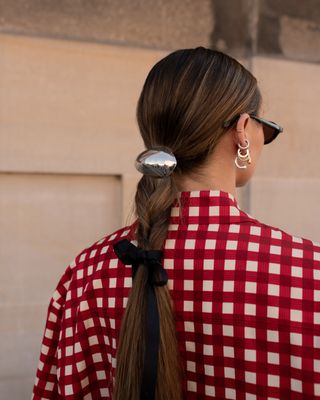 a woman at Copenhagen Fashion Week has a silver charm affixed to her ponytail along with a black bow