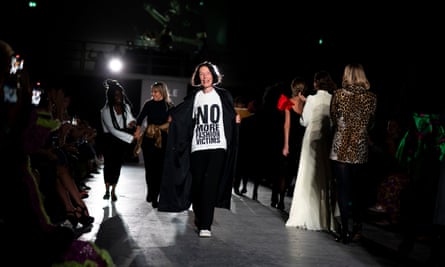 Woman on catwalk wearing black trousers and black coat with a white T-shirt with slogan ‘no more fashion victims’