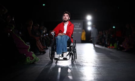 George Robinson in wheelchair on catwalk wearing a red jacket and jeans